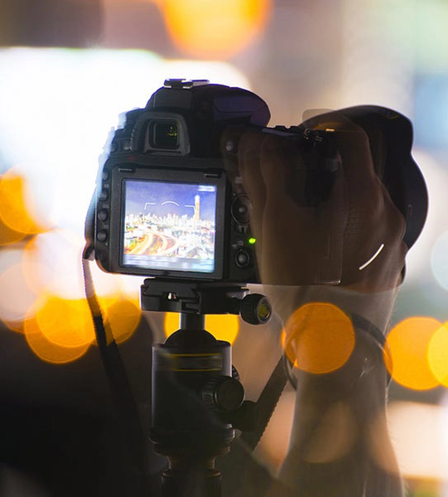 A camera on a tripod, recording a city view in the night.